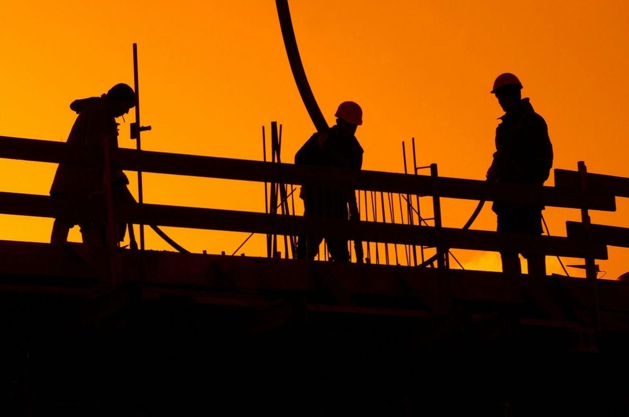 Construction workers silhouetted against an orange sunset